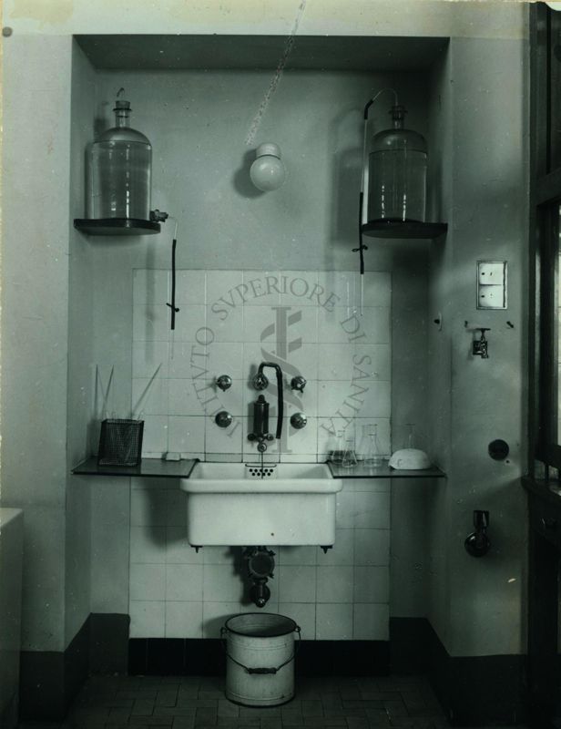 Immagine di un banco di una nicchia con lavandino e boccioni per acqua distillata del laboratorio di chimica dell'Istituto di Sanità Pubblica