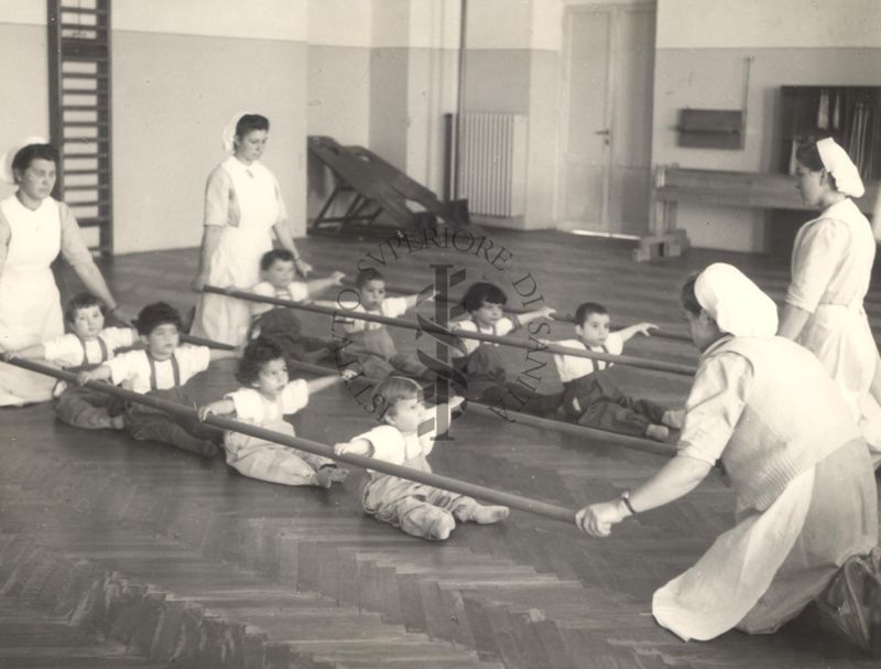 Sala per la ginnastica collettiva dell'Istituto Ortopedico "Luigi Spolverini" di Ariccia (Roma) - delle infermiere sorreggono alcune aste per guidare i movimenti dei bambini