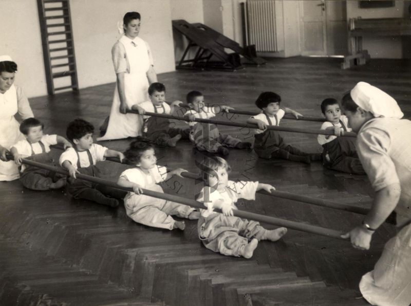 Sala per la ginnastica collettiva dell'Istituto Ortopedico "Luigi Spolverini" di Ariccia (Roma) - delle infermiere sorreggono alcune aste per guidare i movimenti dei bambini