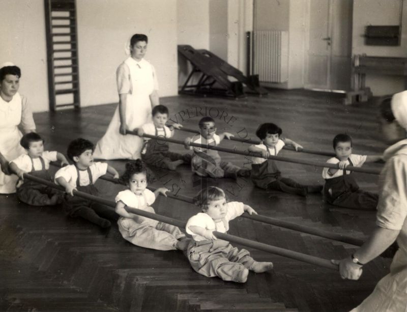 Sala per la ginnastica collettiva dell'Istituto Ortopedico "Luigi Spolverini" di Ariccia (Roma) - delle infermiere sorreggono alcune aste per guidare i movimenti dei bambini