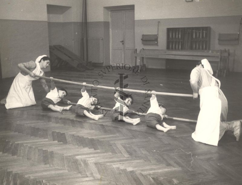 Sala per la ginnastica collettiva dell'Istituto Ortopedico "Luigi Spolverini" di Ariccia (Roma) - delle infermiere sorreggono alcune aste per guidare i movimenti dei bambini