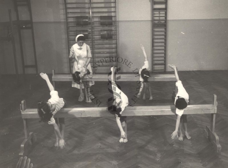 Sala per la ginnastica collettiva dell'Istituto Ortopedico "Luigi Spolverini" di Ariccia (Roma) - un'infermiera controlla la postura di un gruppo di bambini che svolgono esercizi ginnici con l'ausilio di due assi