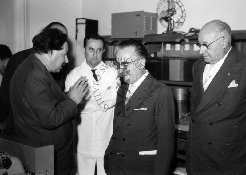 Foto scattata all'interno di uno degli ambienti dell'Istituto Superiore di Sanità, sono presenti da sinistra, il Prof. Ernst Boris Chain che parla con il Ministro della Sanità Vincenzo Monaldi, sulla destra il Prof. Domenico Marotta ed altri