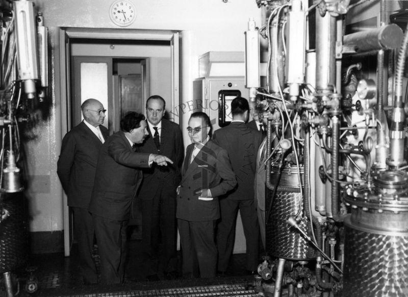 Foto scattata all'interno della fabbirca della Penicillina dell'Istituto Superiore di Sanità nella sala dei fermentatori, sono presenti da sinistra, il Prof. Ernst Boris Chain che parla con il Ministro della Sanità Vincenzo Monaldi, il Prof. Domenico Marotta ed altri