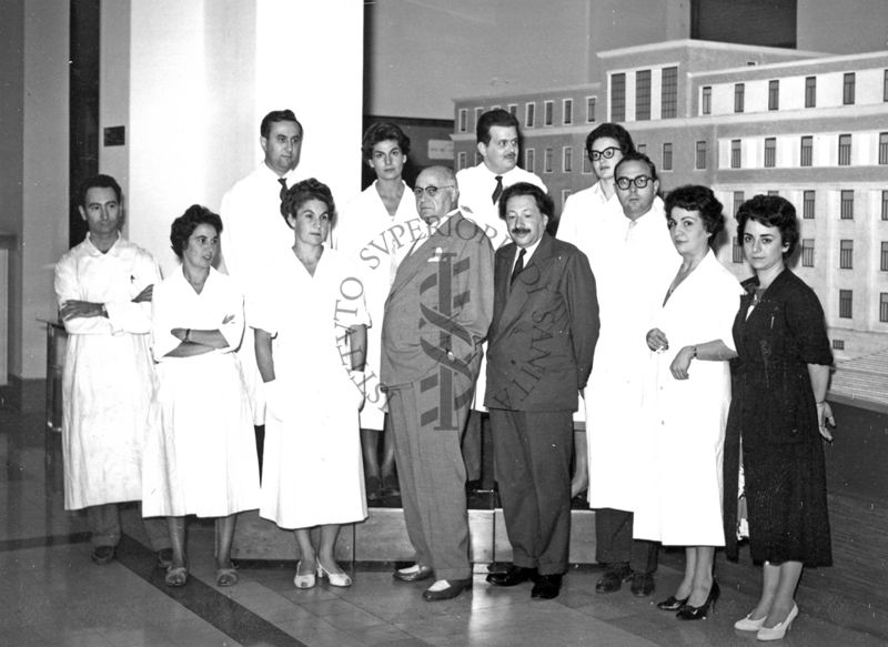 Foto di gruppo del Personale Sanitario e tecnico del Laboratorio di Chimica Biologica nella sala contenente il Plastico dell'Istituto Superiore di Sanità con il Prof. Domenico Marotta e il Prof. Boris Chain