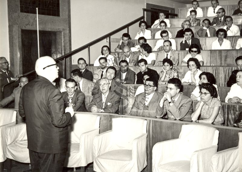 Il Prof. Pomerat in piedi nell'aula si rivolge all'uditorio. In prima fila, sulla sinistra, viene ripreso il Prof. Bovet.