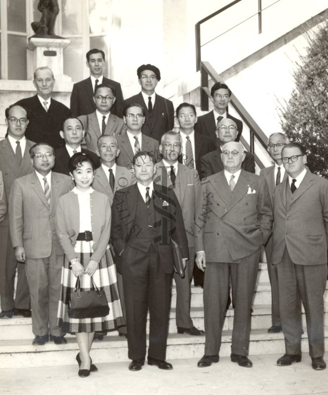 Foto di gruppo degli studiosi giapponesi in visita all'Istituto Superiore di Sanità, disposti su una scalinata, insieme al Direttore Prof. Domenico Marotta (secondo da destra in prima fila), dal Dott. Giuseppe Penso (primo a destra in prima fila) e dal Dott. Massimo Pantaleoni (primo a sinistra in ultima fila)