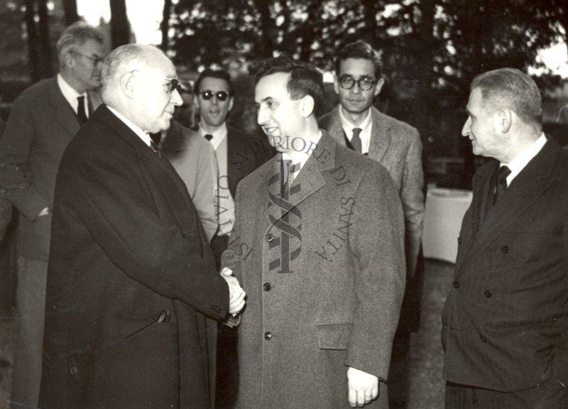 Il Prof. Domenico Marotta (a sinistra) stringe la mano ad un dipendente dell'Istituto Superiore di Sanità, circondato da altri colleghi, nei giardini dell'Istituto