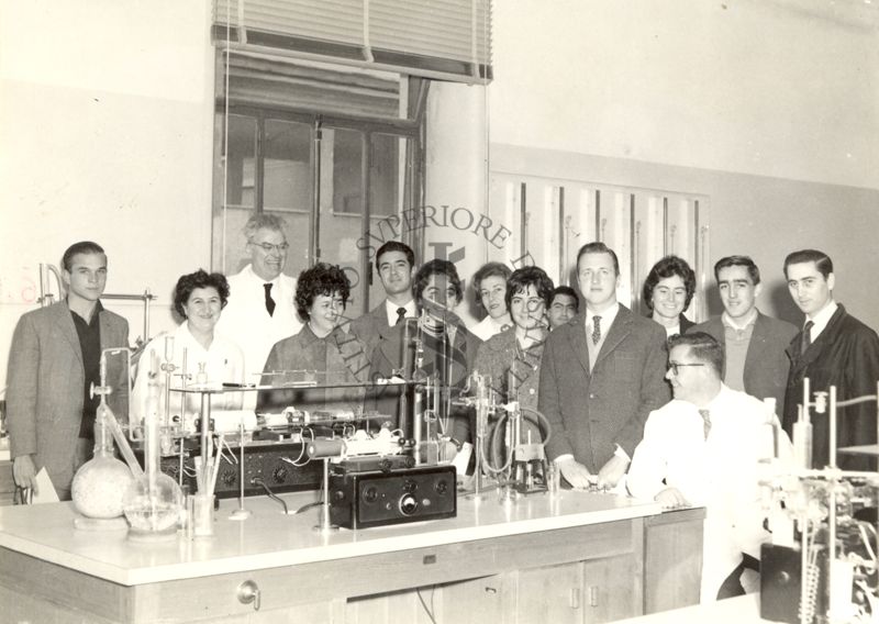 Foto di gruppo con alcuni studenti cileni in visita all'Istituto Superiore di Sanità, il Dott. Marini Bettolo (in camice, sulla sinistra) e altro personale di ricerca in camice intorno ad un bancone di laboratorio dell'Istituto